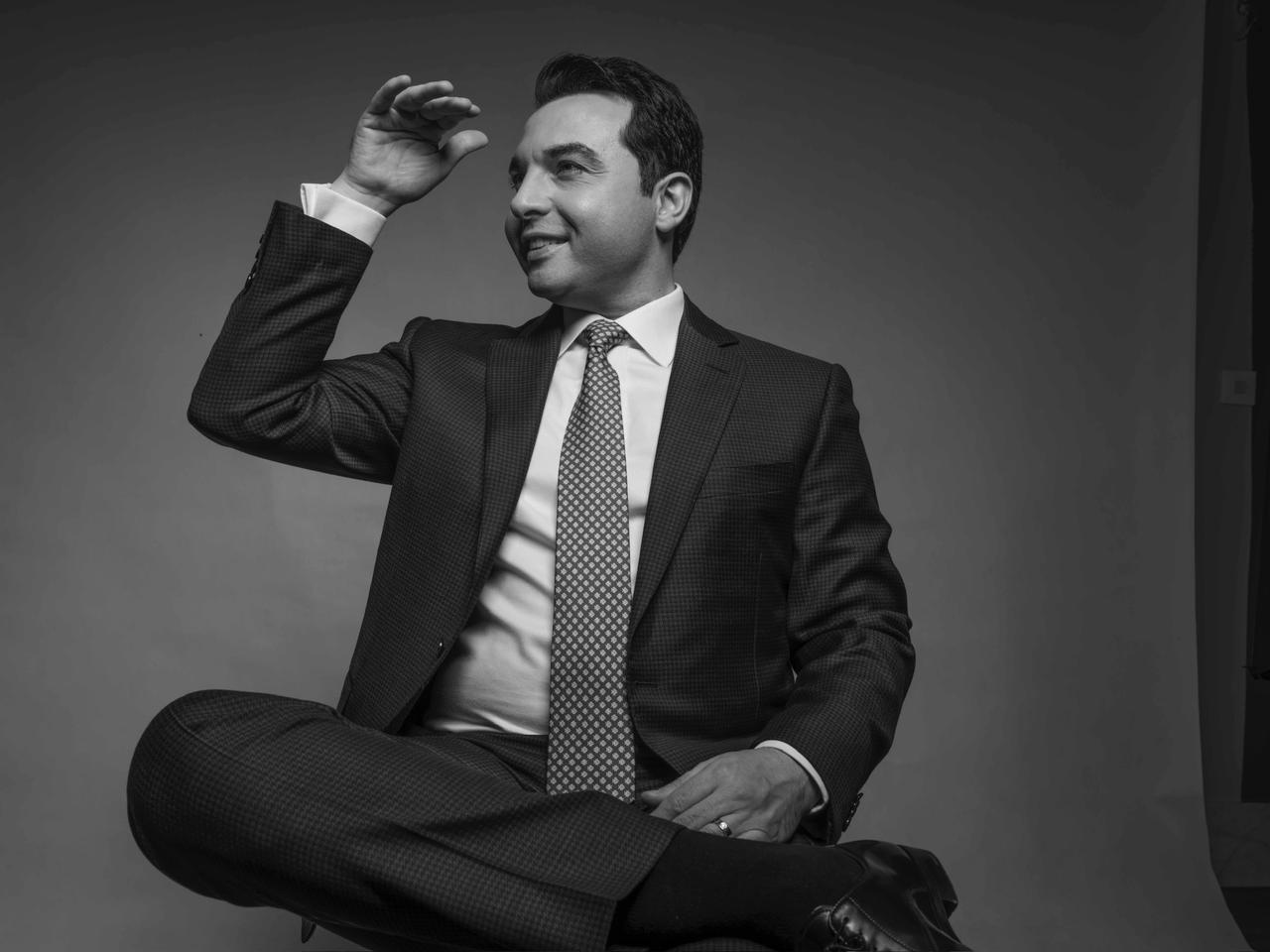 Saied Nazemi — cross-legged in suit, studio portrait